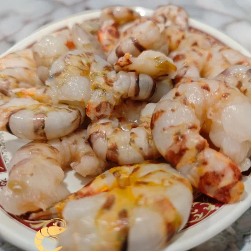 Cola de langostino tigre pelada y descongelada, presentada en plato decorativo, mostrando su textura y frescura. imagen con el logo de Almar y el lema 'Sabor salvaje, alma atlántica' en la parte inferior.